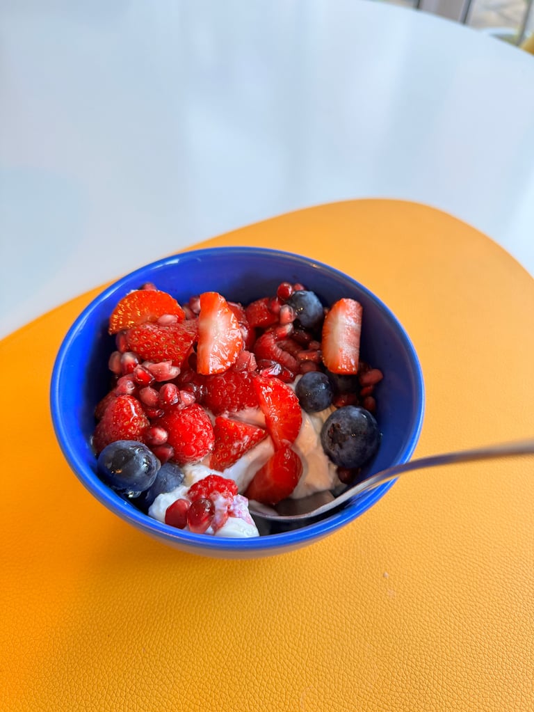 Blue bowl of yogurt with strawberries, blueberries, and granola on a yellow table