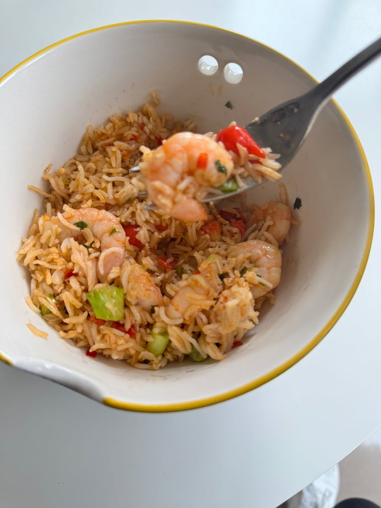 Bowl of shrimp fried rice with red peppers, green vegetables, and a black spoon, garnished with sesame seeds