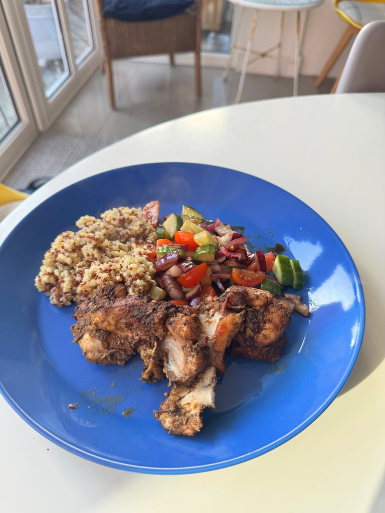 Grilled chicken pieces with quinoa and colorful vegetable medley served on a bright blue plate in a modern dining space